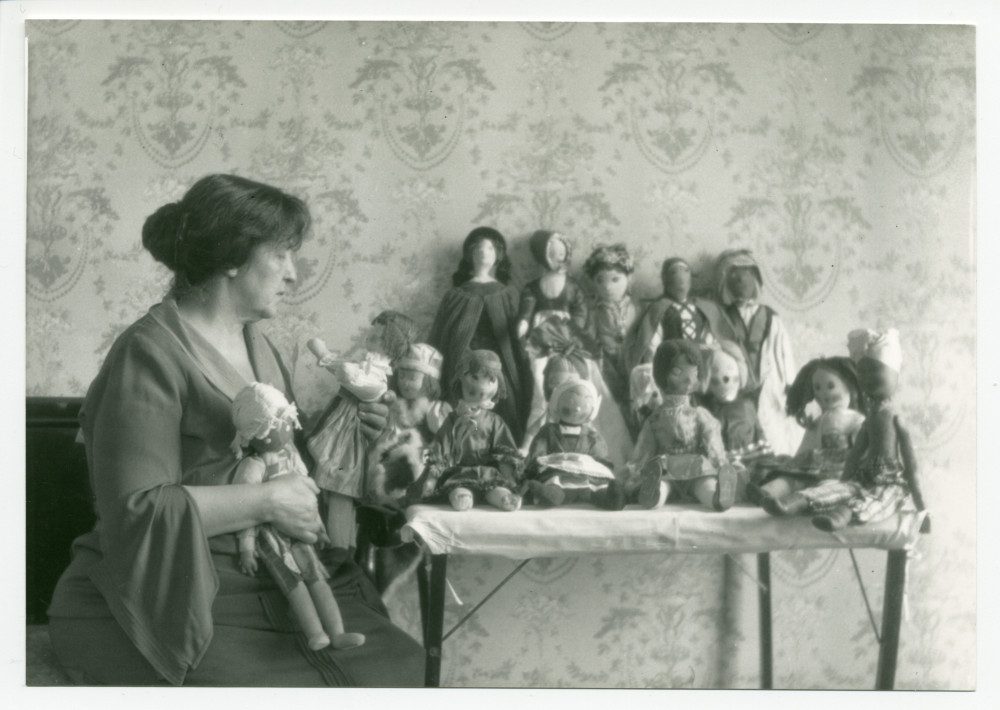 Photographie d'Hélène Paderewska regardant ses poupées (confectionnées durant la Première Guerre mondiale en faveur du «Polish Victim's Relief Fund») posées sur une table dans sa chambre à coucher de Riond-Bosson