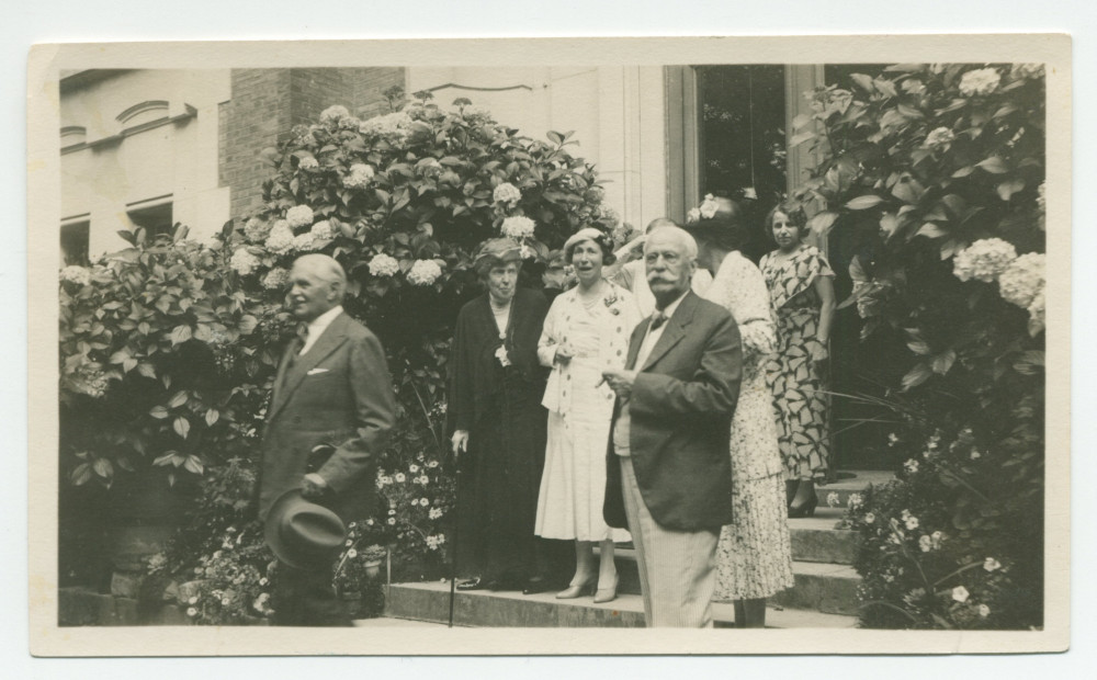 Photographie d'un groupe de personnes sortant de la villa de Riond-Bosson par l'entrée principale, composé entre autres du compositeur Henryk Opienski et d'Henry Vallotton (conseiller national et agent d'affaires de Paderewski, fumant le cigare)