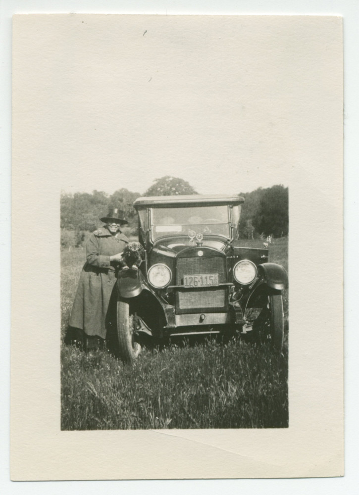 Photographie de la fidèle gouvernante Augusta, avec dans ses bras le chien Ping, à côté d'une voiture, sur les terres du «Rancho Santa Helena» à Paso Robles, en Californie, en mars 1921