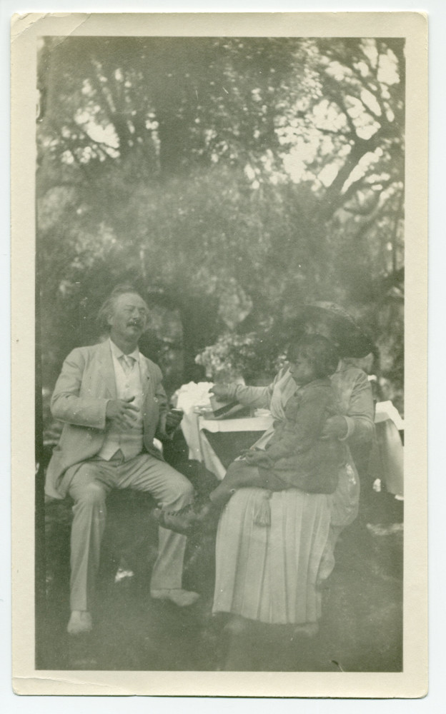 Photographie de Paderewski dans sa propriété de Paso Robles, en Californie, assis (expressif, les yeux clos), avec à sa gauche Hélène Paderewska tenant sur ses genoux Jackie, la fille d'amis américains, en 1921