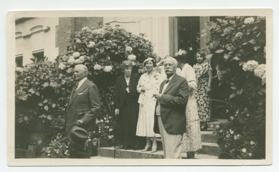 Photographie d'un groupe de personnes sortant de la villa de Riond-Bosson par l'entrée principale, composé entre autres du compositeur Henryk Opienski et d'Henry Vallotton (conseiller national et agent d'affaires de Paderewski, fumant le cigare)