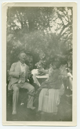 Photographie de Paderewski dans sa propriété de Paso Robles, en Californie, assis (expressif, les yeux clos), avec à sa gauche Hélène Paderewska tenant sur ses genoux Jackie, la fille d'amis américains, en 1921