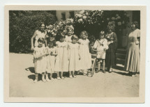 Photographie d'un groupe de jeunes filles en robes blanches (dont Anne Strakacz, à droite) et d'Ignace Obuchowicz (filleul de Paderewski) en costume de marin, avec sa mère Barbara, devant l'entrée principale de Riond-Bosson