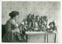 Photographie d'Hélène Paderewska regardant ses poupées (confectionnées durant la Première Guerre mondiale en faveur du «Polish Victim's Relief Fund») posées sur une table dans sa chambre à coucher de Riond-Bosson